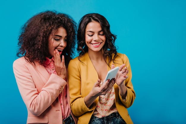 Cheerful latin girl with wavy hairstyle making selfie Glamorous friends chilling in studio