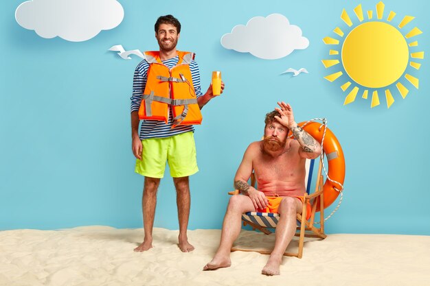 Cheerful lifeguard and sunburnt guy posing at the beach