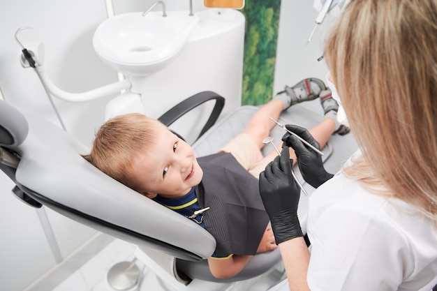 Веселый маленький мальчик сидит в стоматологическом кресле в стоматологическом кабинете