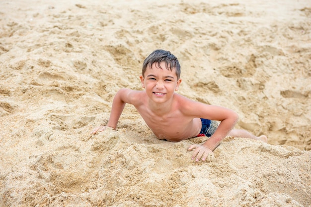 Cheerful little brunette boy on the beach plays with sand baby travel concept holidays at sea