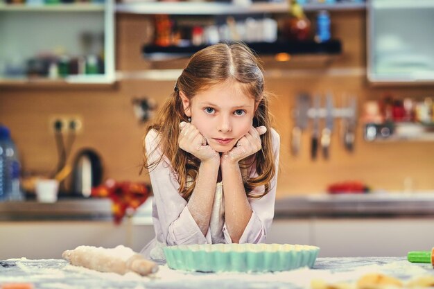 Cheerful little girl cooking dough at the kitchen.