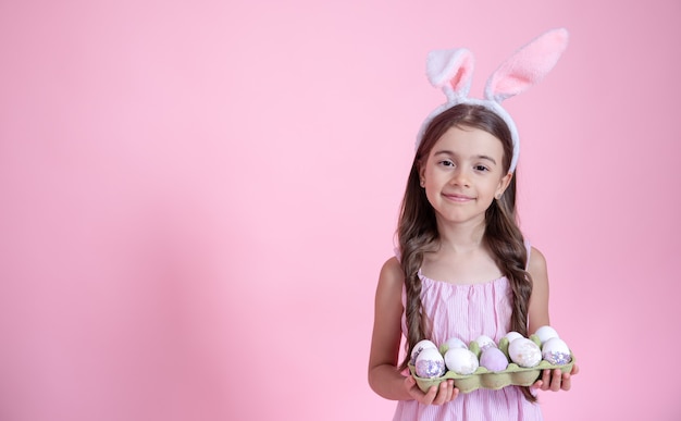 부활절 토끼 귀와 분홍색 벽에 그녀의 손에있는 계란 트레이 명랑 소녀. 부활절 휴가 개념.
