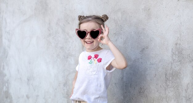 Cheerful little girls on gray textured background. Outdoor portrait little girl. Gray textured wall background.