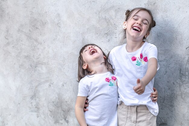 Cheerful little girls on gray textured background. Outdoor portrait little girl. Gray textured wall background.