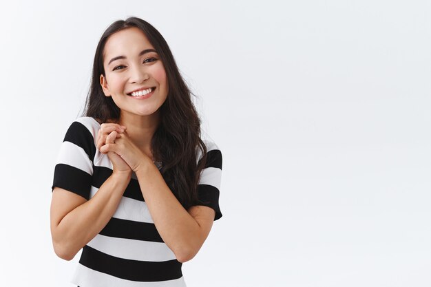 Cheerful, lovely feminine girl smiling happy, clasp hands together near shoulder, tilt head cute and grinning, sighing as gazing with admiration and gratitude, standing grateful white background