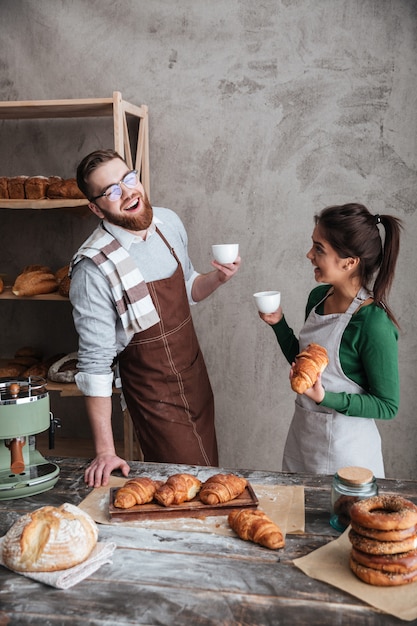 Cheerful loving couple bakers drinking coffee. Looking aside.