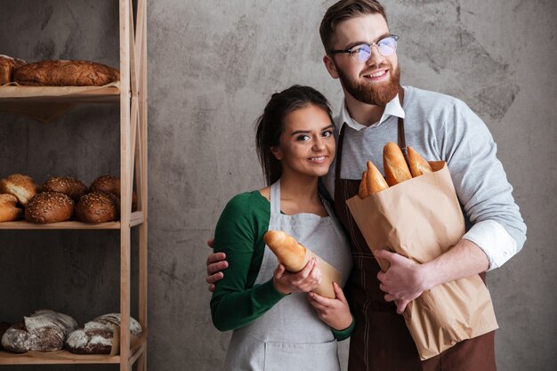 Cheerful loving couple bakers holding bread in hands.