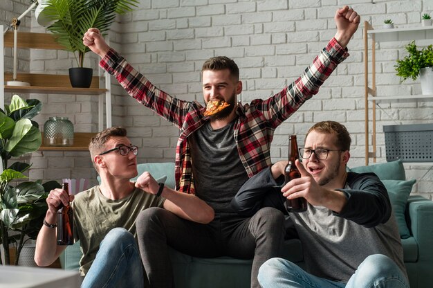 Cheerful male friends having pizza and watching sports on tv