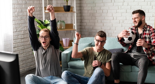 Cheerful male friends watching sports on tv with football and beer