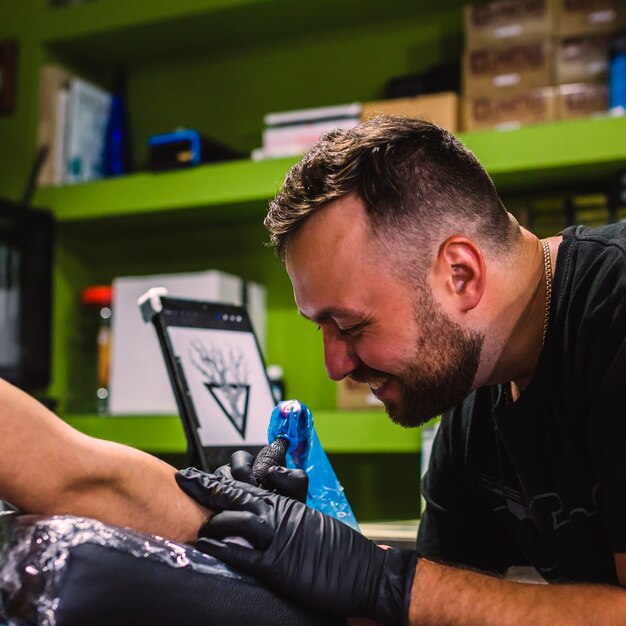 Веселый человек делает татуировку в перчатках в студии