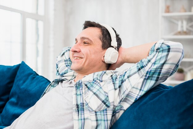 Cheerful man listening music in headphones on sofa