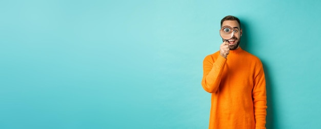 Free photo cheerful man searching for something looking through magnifying glass and smiling happy standing ove