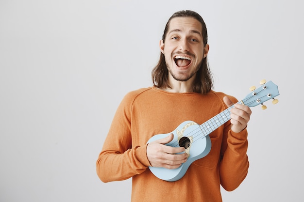 Веселый человек поет песню и играет на укулеле со счастливым выражением лица