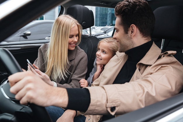 Uomo allegro che si siede in automobile con sua moglie e figlia