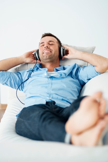 Free photo cheerful man wearing headphones lying on the sofa