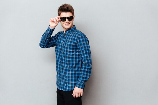 Cheerful man wearing sunglasses standing over grey wall