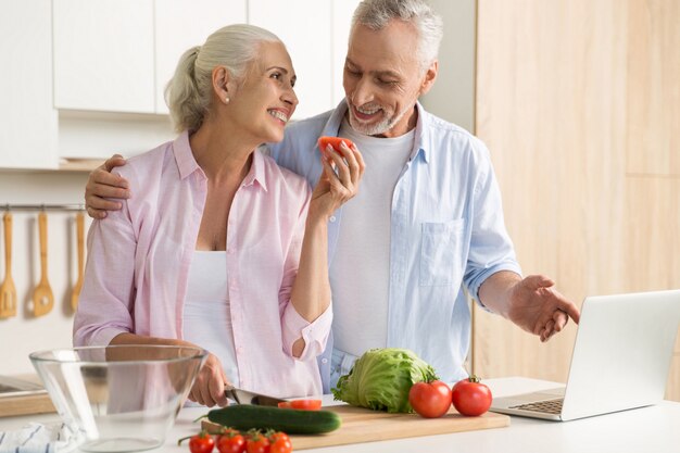 Cheerful mature loving couple family using laptop and cooking