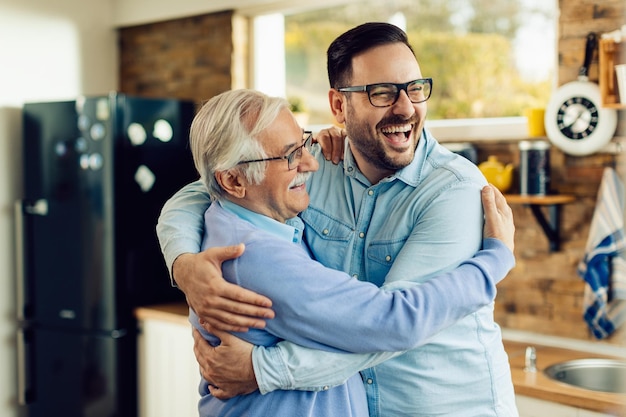 Foto gratuita uomo maturo allegro e suo figlio adulto che si abbracciano mentre salutano in cucina