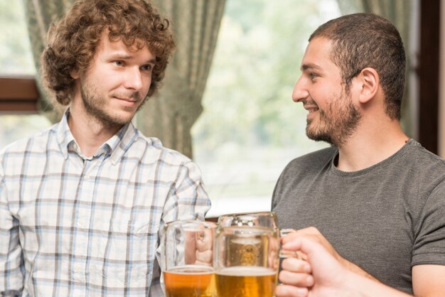 Cheerful men clinking mugs in bar