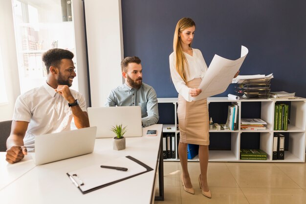 Cheerful men looking at woman with blueprint