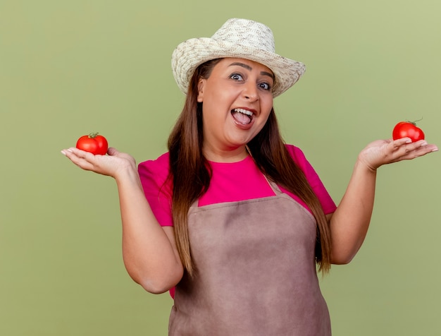 Веселая женщина-садовник средних лет в фартуке и шляпе держит свежие помидоры