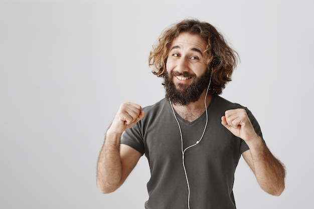 Cheerful middle-eastern guy listening music in earphones and dancing