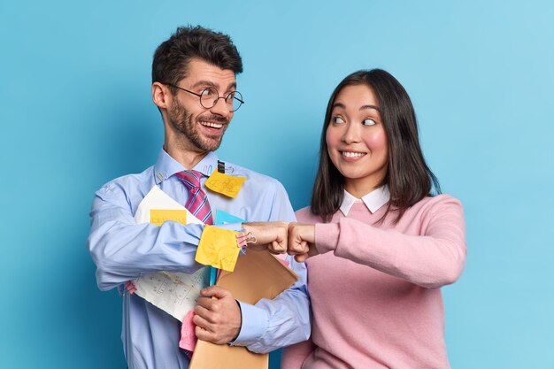 Cheerful mixed race woman and man colleagues celebrate successfully finished work make fist bump pose with paper documents look gladfully at each other 
