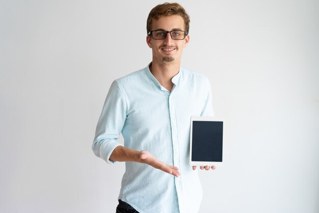Веселый разработчик мобильных приложений в очках, показывающий экран планшета и глядя на камеру.