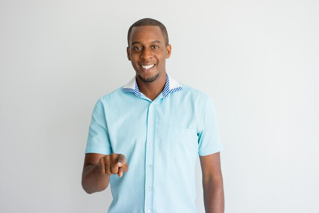 Cheerful modern guy pointing with index finger and looking at camera. 