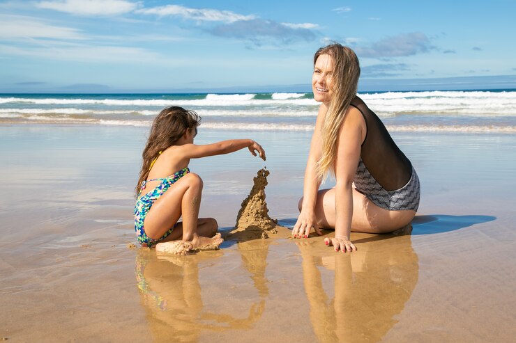 Free Photo cheerful mom and little daughter building sandcastle on beach, sitting on wet sand, enjoying vacation at sea