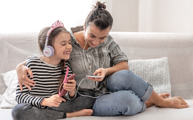 Cheerful mother and daughter are resting at home, listening to music on headphones