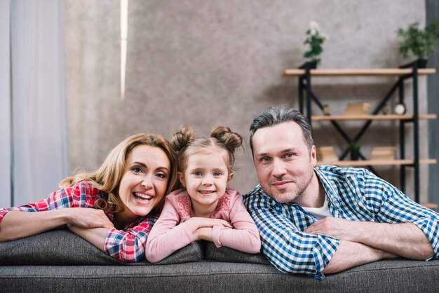 Cheerful mother; daughter and father sitting on sofa looking at camera