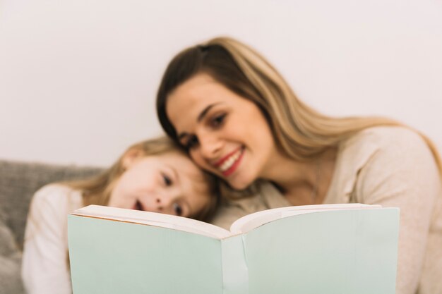 Cheerful mother reading book with daughter