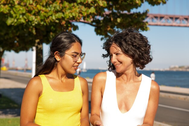 Cheerful multiethnic women walking at riverside