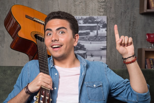 Cheerful musician holding a beautiful guitar and sitting on sofa. High quality photo