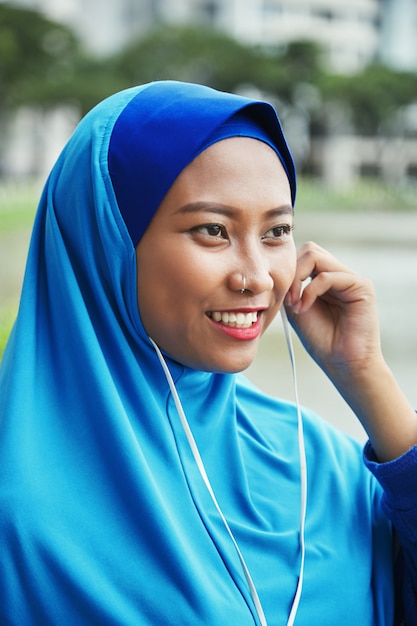 Cheerful Muslim woman in earphones