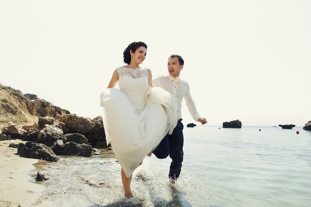 Cheerful newlyweds run along the beach