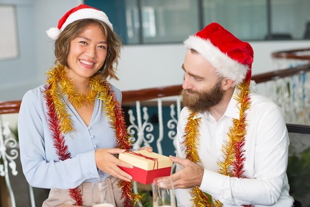 Cheerful office assistant in Santa hat giving Christmas gift