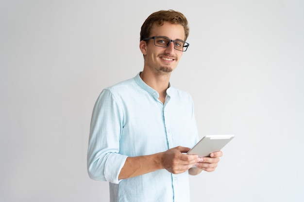Cheerful optimistic handsome male manager using tablet and looking at camera. 