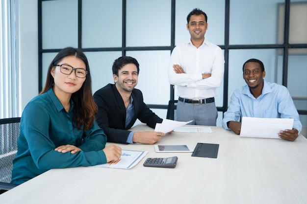 Cheerful optimistic sales managers analyzing report and looking at camera in board room.