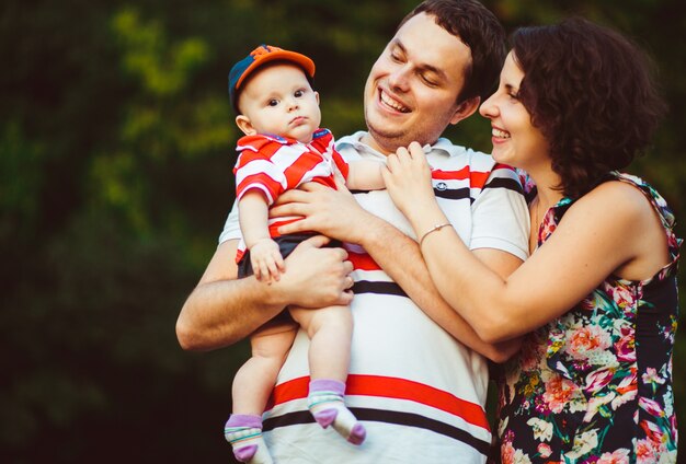 Cheerful parents smile to little son on their arms