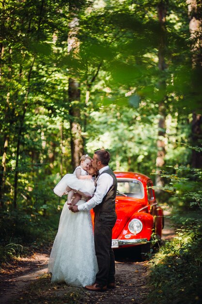 Cheerful parents walk with their little daughter before old-fashioned car 