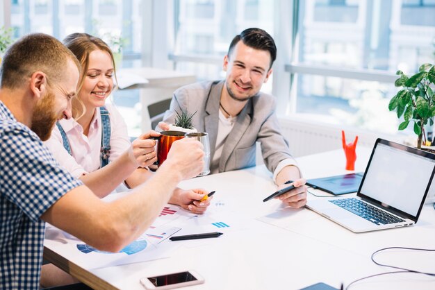 Cheerful people clinking cups while working