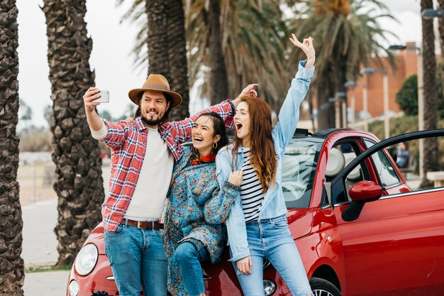 Cheerful people taking selfie near red car in street