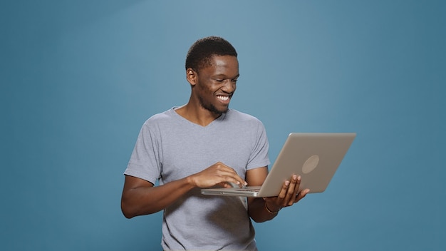 Веселый человек просматривает интернет на ноутбуке в студии, используя портативный электронный компьютер для навигации по социальным сетям и сети онлайн-сайтов. Счастливый человек, держащий беспроводной гаджет.