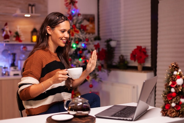 Cheerful person holding cup of tea while on video call