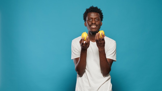 健康的な菜食のためにレモンを持っている陽気な人。ビタミンと自然な栄養のために手に黄色の柑橘系の果物を提示する男。新鮮なジューシーなフルーツをカメラに向ける大人のハウリング
