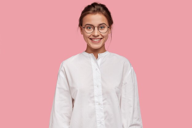 Cheerful pleasant looking woman in eyewear, has happy expression, dressed in white shirt