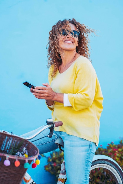 携帯電話を使用して自転車に乗って幸せな若い大人の女性の陽気な肖像画。スマートフォンの携帯電話アプリケーションで現代のオンライン接続された女性 Premium写真