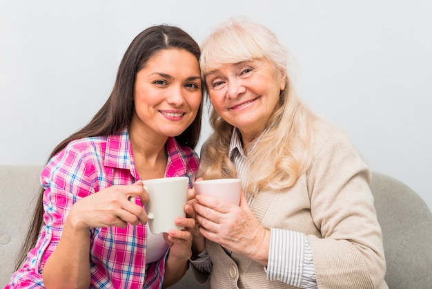 母と大人の娘のコーヒーマグカップを手で押しの陽気な肖像画